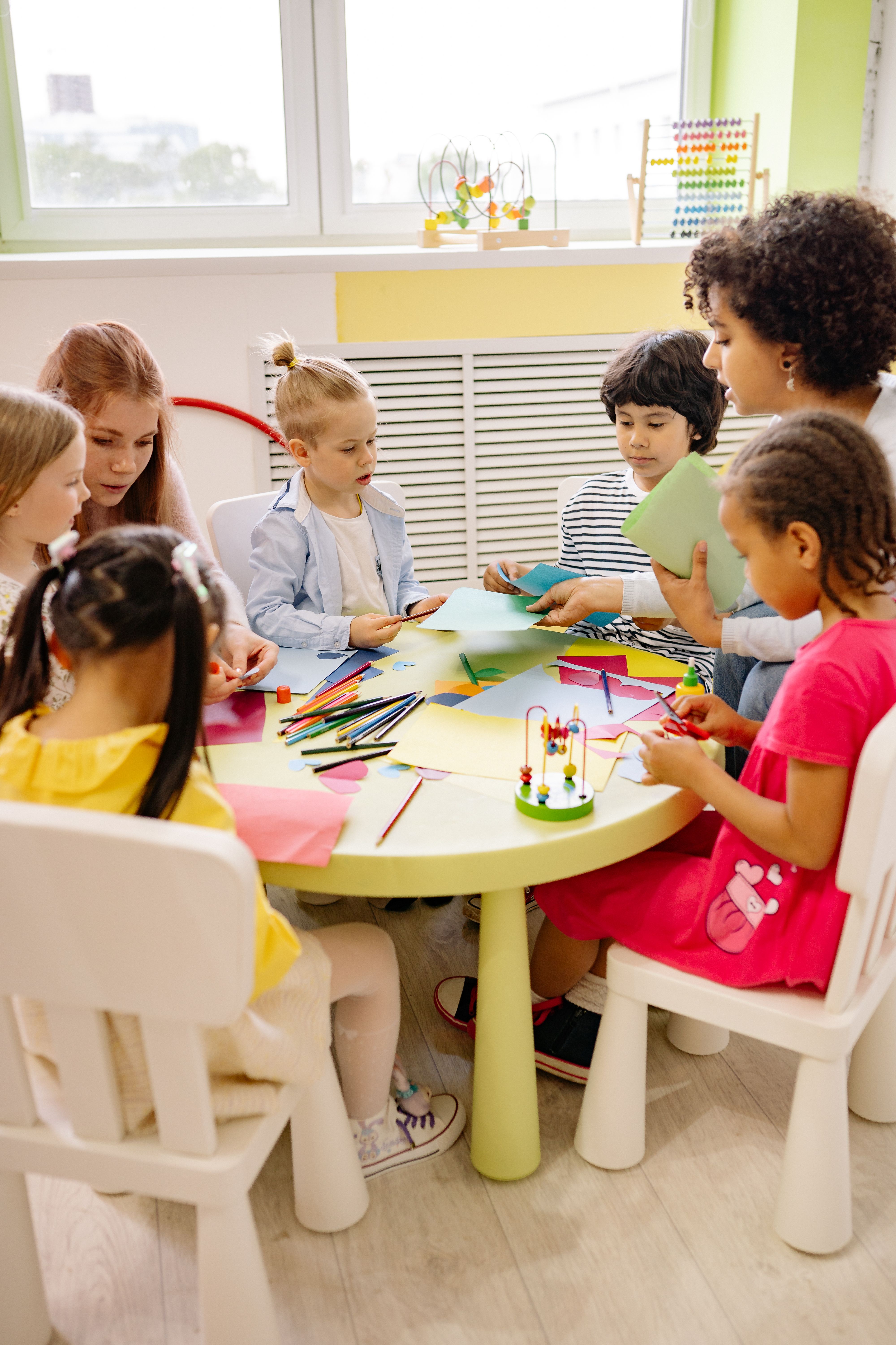 Children working together on a colorful craft project at a round table with a teacher guiding them