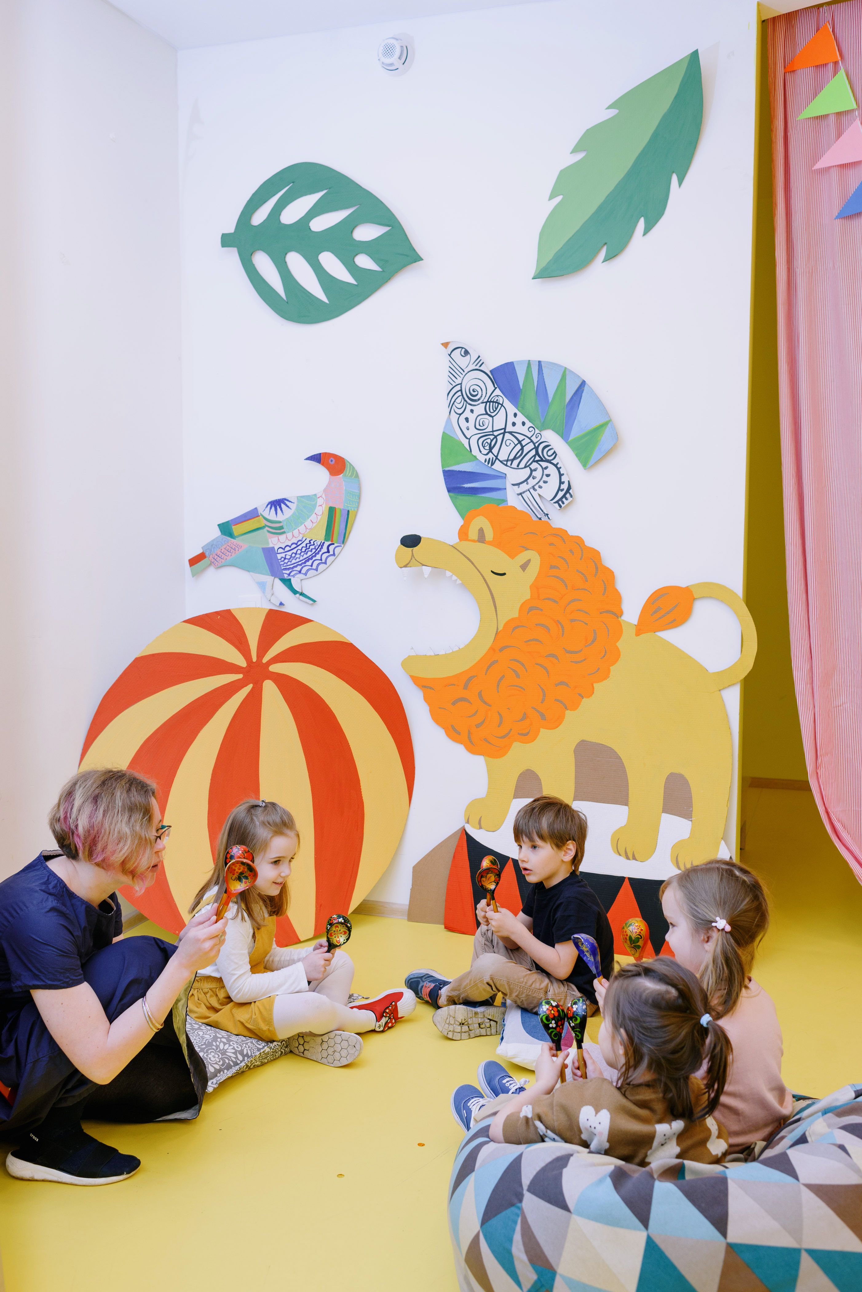 Warm, colorful daycare play area with children and a teacher sitting on the floor surrounded by bright toys